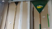 Photo showing four garden tools hung in a garage: two rakes with green heads and two hoes with wooden handles and metal blades
