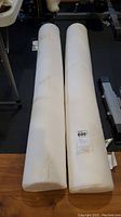 Two white safety bed pillows placed side by side on a wooden floor, showing length and shape