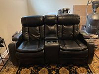 Front view of black leather motorized loveseat showing two seating positions, center console, padded armrests and headrests.