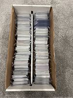 Top-down view of a two-row cardboard box filled with NBA basketball cards. Cards are individually sleeved in clear plastic.