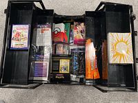 Top-down view of the open black plastic carrying case filled with multiple Pokémon trading card related items including booster packs, card binders, and card sleeves in compartments.