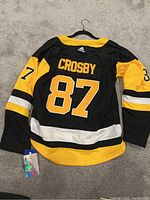 Photo showing back of the Adidas black and yellow Pittsburgh Penguins NHL jersey featuring Crosby name and number 87, along with Adidas tag indicating new condition.