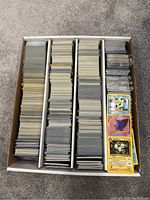 White cardboard storage box with four rows filled with assorted Pokémon trading cards