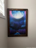 Framed painting showing Eevee looking at a large moon with a vibrant night sky in the background, placed leaning against a wall near a window