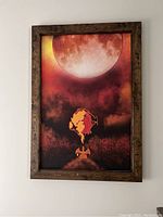 Photo of framed painting showing a large red moon at the top and a silhouette of a Pokémon character below it.