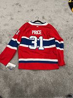 Back view of a red Montreal Canadiens hockey jersey with player name 'Price' and number 31 in white and navy blue, laid flat on grey carpet.