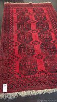 Full view of red wool rug with black geometric pattern and fringe