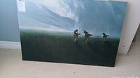 Full view of rectangular artwork print on wood showing three black horses running across a field with a cloudy sky background.