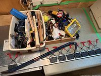 Photo showing a variety of tools including a circular saw, cordless drill, clamps in a bin, portable work light, and more items in boxes.