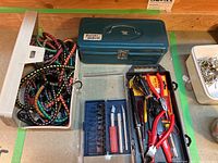 Photo showing metal toolbox, bungee cords, clear plastic case with carving blades and handles, and a container with picture hanging supplies.
