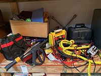 Wide view of lot showing assorted automotive accessories such as rope, jumper cables, car brush, and tool bag spread on wood shelf.