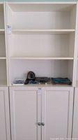 Front view of white bookcase showing two open shelves and lower cabinets with round metal knobs.