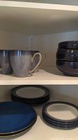 Top shelf showing 3 bowls stacked and several mugs and plates below them