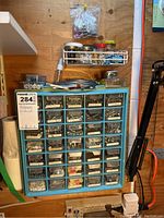 Full view of blue storage cabinet filled with assorted metal fasteners and small hardware components, jars and small containers on and above the cabinet.