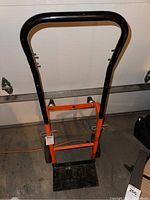 Full front view of the hand cart showing orange metal frame, black handle, and flat base plate.