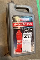 Closed grey plastic carry case with label showing red hydraulic jack with 4 ton capacity and lift range.