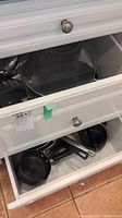 Two open drawers filled with various pots, pans, baking pans, and glass lids with metal handles.