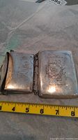 Two silver cases side by side on paper, showing overall size against ruler (approx. 3″ wide each).