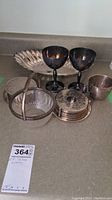 Wide view of all silverware items including goblets, coasters in holder, glass bowl with handle, small mug, and serving dish.