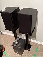 Front view of two black Phase Technology PC 80 bookshelf speakers on black metal stands with a black Phase subwoofer below them.