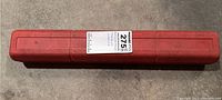 Closed red plastic case of the torque wrench with a label.