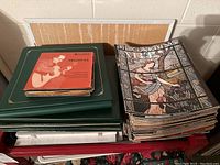View showing stack of vintage vinyl records and a large stack of Art magazines on red trolley cart with bulletin board behind