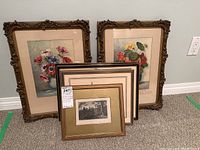 Five vintage framed art prints grouped together. Two large floral prints with vibrant flowers in ornate carved bronze-gold frames. Three smaller framed black and white prints with maritime and landscape themes.