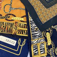 Close-up of folded scarves showing Gucci logos and chain-link and animal print motifs