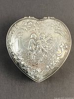 Top view of heart-shaped lid showing repoussé cherub scene under a tree with scrollwork border