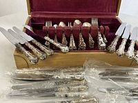 Overview of wooden case open showing velvet-lined insert with flatware arranged and additional knives unpackaged in front