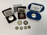 Overview of 10 coins including commemorative coins in cases and loose coins on surface