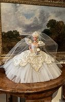 Doll posed in front of framed artwork to show full gown and headpiece