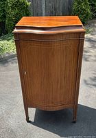 Front view of the wooden music cabinet showing inlaid wood pattern on door and brass lock.