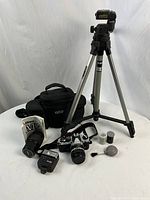 Full kit laid out on table: tripod extended, camera bag behind, camera with lens attached, manual, flash, lens, canisters and blower brush