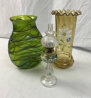 All three pieces displayed on neutral backdrop: green Loetz vase, yellow enameled vase, and miniature oil lamp