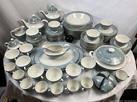 Full overview of dinner and tea service arranged on table: bowls, plates, cups, pots