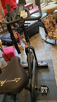 Stationary Bowflex exercise bike on black mat with red strap attached to handlebars and Pearl Izumi shoes placed on floor