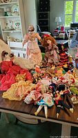 Wide view of the collection of various dolls laid out on a table showing mixed styles, sizes and outfits