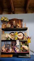 Shelf with various figurines, tins, faux flowers, plaques including butterfly decor and owl figurine