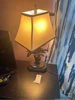 Lamp lit on dark wooden surface with beige fabric shade and multi-leaf metal base