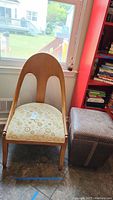 Side view of the wooden framed chair with curved backrest and floral upholstered seat next to the leather-like ottoman.