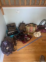 Photo showing an overview of purses and totes in different shapes, sizes, and materials arranged on the floor including backpacks, handbags, totes, and clutches with various patterns including leopard print, stripes, floral, and sequins.