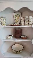Wide shot showing entire pottery set including mugs, bowls, plates on shelf