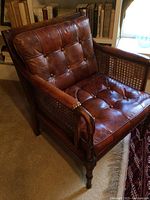 Front and left-side view of one armchair showing tufted leather seat and back, cane side panel and turned wood leg.
