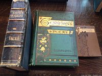 Three antique books displayed on a surface: a large bound Harper's Magazine volume, Tennyson's Poems Illustrated in green cover, and Bryant's Poems brown hardcover.