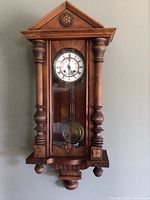 Front view of antique grandmother wall clock, showing wooden case, columns, and clock face with glass door closed.