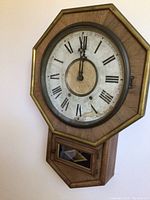 Full view of antique octagon-shaped wall clock with Roman numerals, gold trim, and wooden frame.