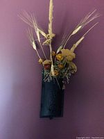 Wall mountable cast iron mailbox serving as a vase with dried flower arrangement against a purple wall.