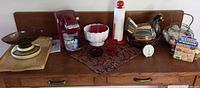Wide shot of all items on a wooden sideboard including kitchen scale, Keurig coffee maker, milk glass bowl, ceramic chicken cookie jar and more