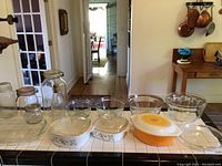 Wide view of lot on tiled kitchen counter showing all glassware, bowls, dishes, jars and bottles